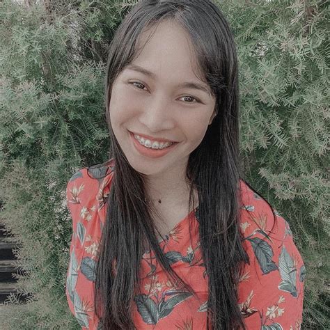 A Woman With Long Hair Standing In Front Of Some Bushes And Trees