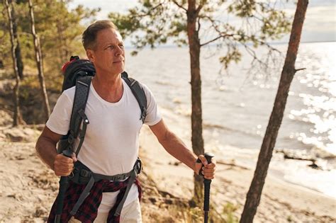 Premium Photo Happy Mature Male Is Going Nordic Walking With Sticks Through Wood Above Sea