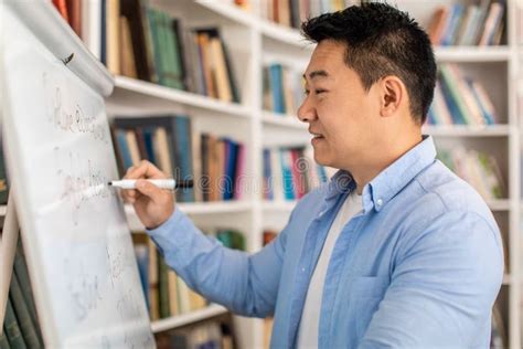 Happy Korean Male Teacher Writing On Whiteboard Standing In Classroom