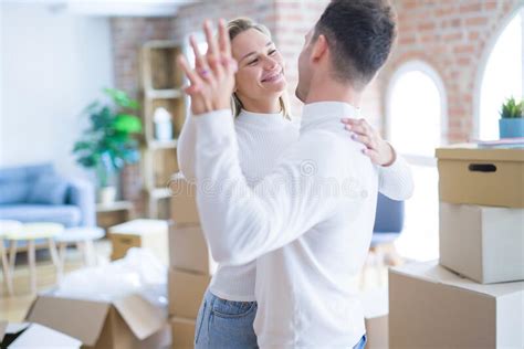 Young Beautiful Couple Dancing At New Home Around Cardboard Boxes Stock