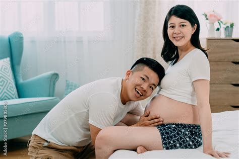 Happy Pregnant Wife Sitting In Bed With Her Husband In Bright Bedroom