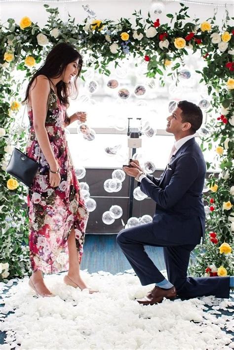 A Man Kneeling Down Next To A Woman In A Dress And Holding A Wine Glass