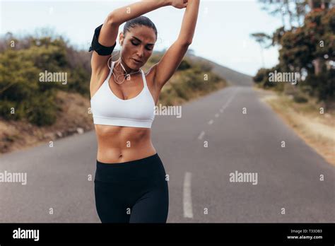 Sporty Woman Stretching Her Arms While Walking On A Empty Road In