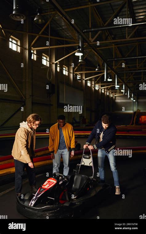 Happy Interracial Friends Standing Near Red Go Kart Inside Of Indoor