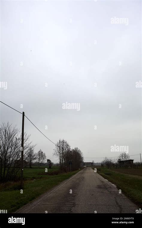 Empty Road With Wooden Poles At Its Edge And Fields Bordering It On A