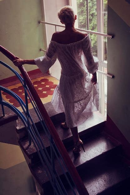 Premium Photo Blonde Woman In A White Semitransparent Dress Climbs The Stairs In The Entrance