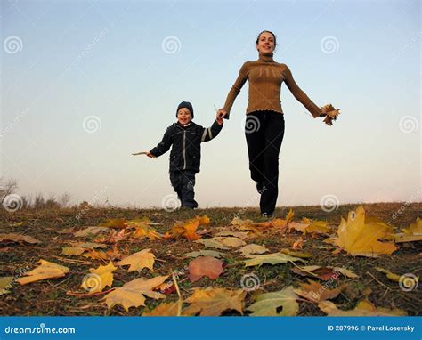 Madre Que Recorre Con El Hijo En Las Hojas De Otoño Foto de archivo