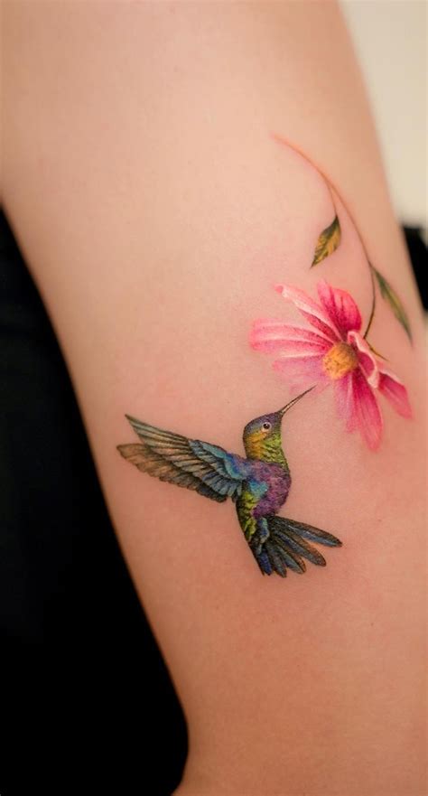 A Hummingbird Flying Towards A Flower On The Back Of A Woman S Shoulder