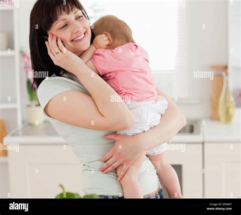 Lovely Brunette Woman On The Phone While Holding Her Baby In Her Arms
