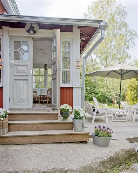 A Porch With Flowers And An Umbrella In Front Of The Door To A Small House