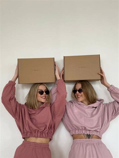 Two Women In Matching Outfits Hold Up Boxes Above Their Heads Both