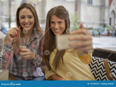 Two Joyful Cheerful Girls Taking A Selfie While Sitting At Cafe Stock