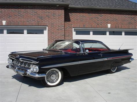 an old black car parked in front of a garage