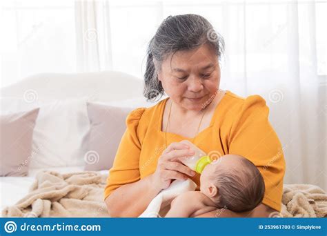 Asian Grandmother Feeding Newborn Baby In Bedroom Senior Women Taking