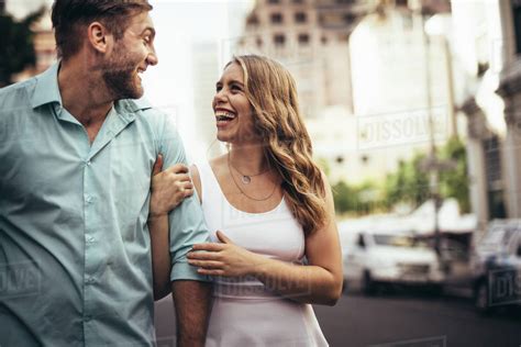 Cheerful Couple Walking On City Street Laughing And Looking At Each Other Woman Holding Her