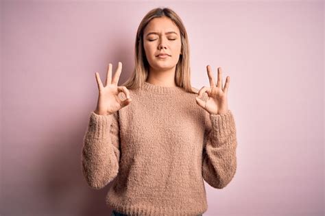 분홍색 고립 된 배경에 겨울 울 스웨터를 입고 젊은 아름다운 금발 의 여자는 편안하고 손가락으로 명상 제스처를하고 눈을 감고