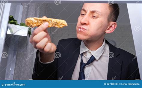 Hungry Businessman Eats Cucumber With Cakes In Dark Kitchen Stock Photo