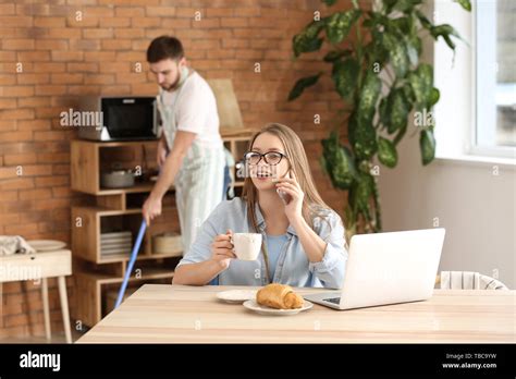 Busy Wife Working While Her Husband Doing Chores At Home Stock Photo