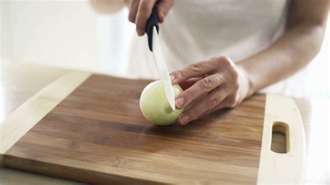 Woman slicing onion on chopping board in kitchen, slow motion shot at ...