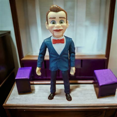 a toy man in a blue suit and red bow tie stands on a table with purple ...