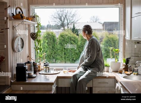 Mature Woman Sitting On Kitchen Counter At Home Looking Out Of Window