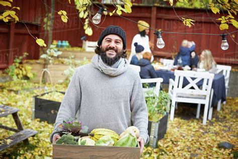 Portrait of happy man standing with vegetable basket while family and ... 