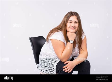 Portrait Of A Smiling Casual Blonde Caucasian Overweight Plus Size Woman Sitting On A Chair