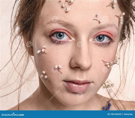 Portrait Of Young Woman With Flowers On Face Against White Background