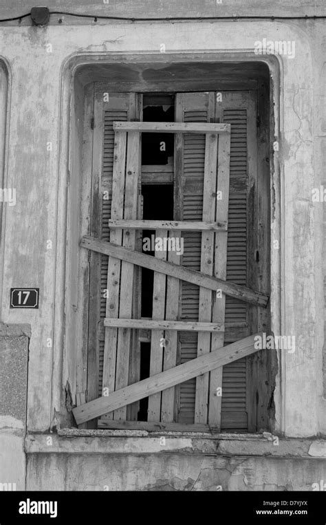 Broken Window Shutter Sealed With Planks And Weathered Wall Of