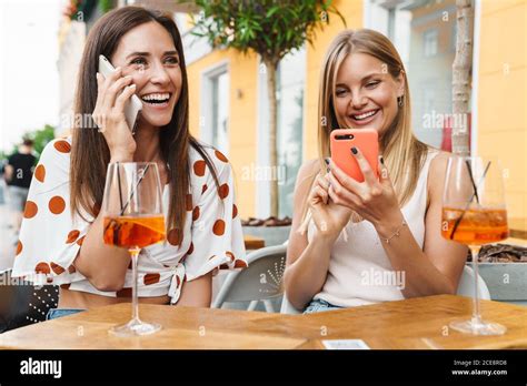 Image Of Joyful Adult Two Women Laughing And Using Cellphones While