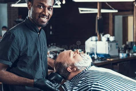 Maestro Barbero Parado Cerca Del Cliente Y Sonriente Imagen De Archivo