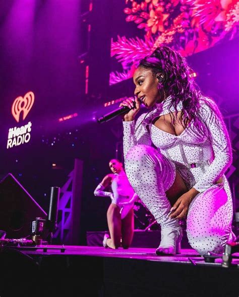 a woman in white outfit standing on stage with microphone and purple ...