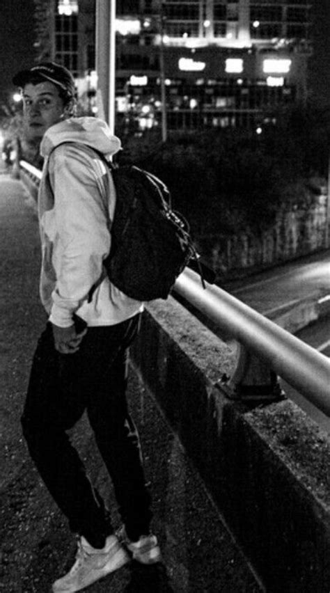 A Man With A Backpack Leaning On A Railing At Night In Front Of A Cityscape