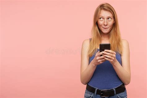 Positive Young Lovely Long Haired Redhead Lady In Blue Shirt Keeping Mobile Phone In Her Hands