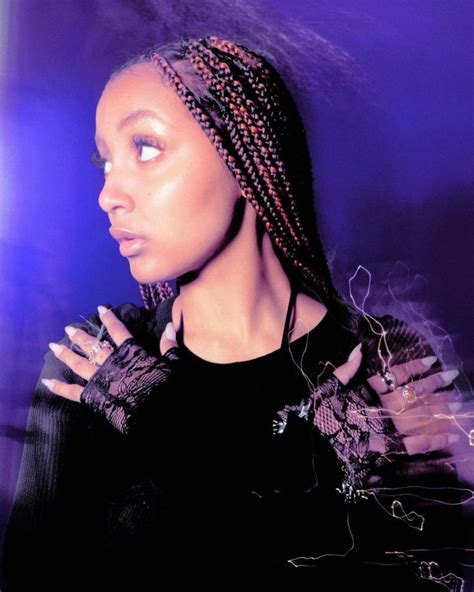 A Woman With Braids Standing In Front Of A Purple Background