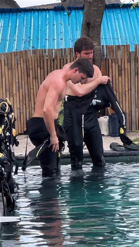 Two Men In Wetsuits Are Standing In The Water With Their Arms Around