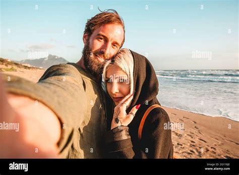 Traveling Couple In Love Taking Selfie In A Deserted Beach At Sunset