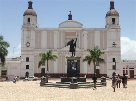 People Are Walking Around In Front Of A Large Building With A Statue On