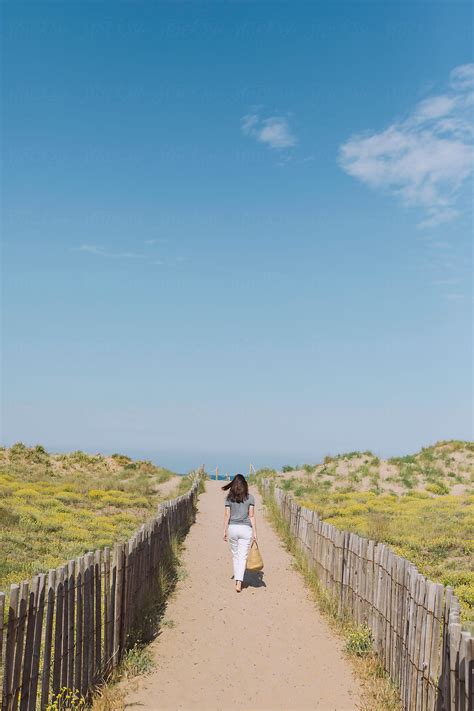 «woman Walking On The Sand Path To The Beach With Yellow Flowers Del