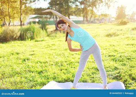 Jovem Mulher Que Faz a Ioga Que Estica Exercícios Na Grama Foto de