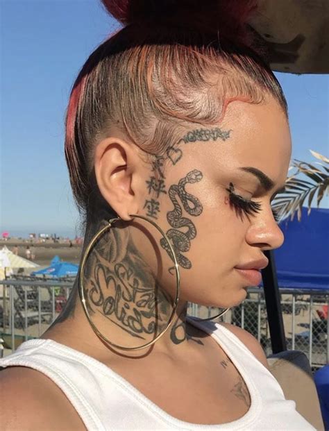 A Woman With Tattoos On Her Face And Ear Is Looking Down At The Ground