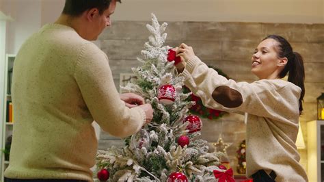 Beautiful Wife And Her Husband Hanging Globes In Christmas Tree Celebrating Christmas