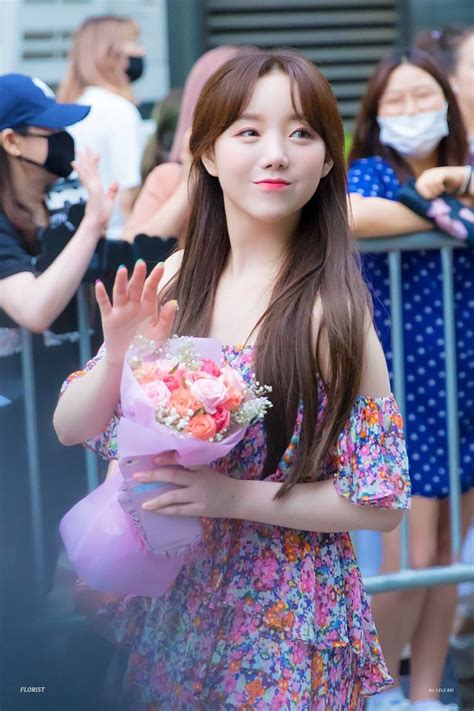 A Woman In A Floral Dress Holding Flowers And Wearing A Face Mask While