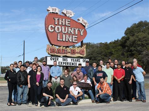 a group of people posing in front of the county line bar - b - q sign