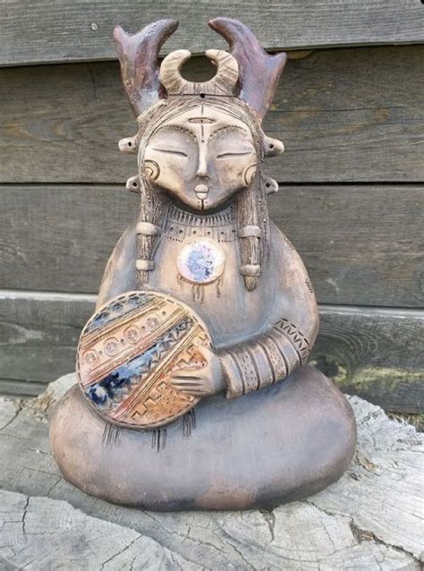 A Statue Of A Woman With Horns On Her Head Is Sitting On Top Of A Rock