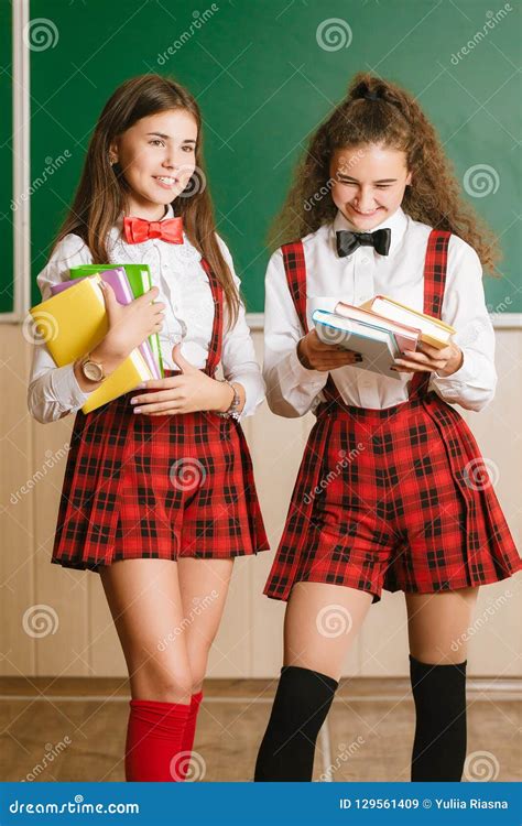 Two Funny Schoolgirls In School Uniform Are Standing With Books On The