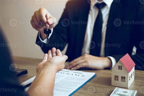 Hand Of Real Estate Agent Passes The Key To New Homeowners In Office With Buyer House Concept