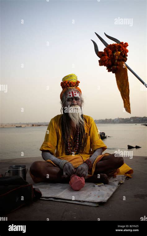 An Indian Sadhu Man Sits In Meditation Posture Near The Bank Of The