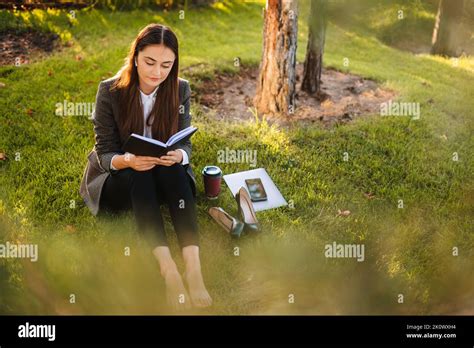 Smiling Beautiful Brunette Woman Sitting On The Green Grass Reading