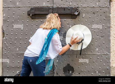 Blonde Woman With A Straw Hat In Her Hand Spies From The Keyhole Of An Ancient Door Stock Photo